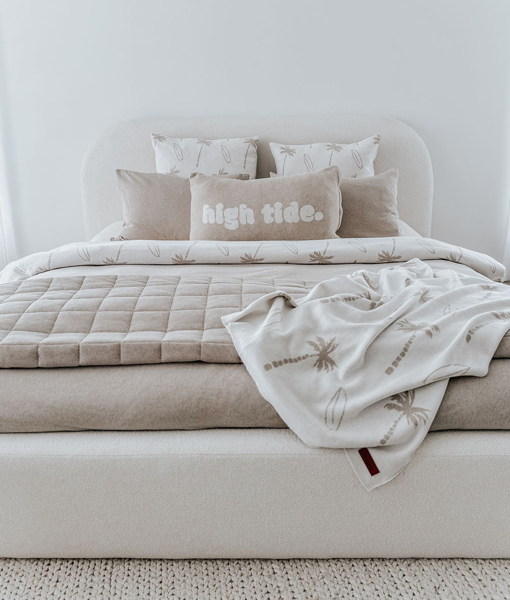 Bed with a high tide cushion, the dune quilt and a palm print throw folded across