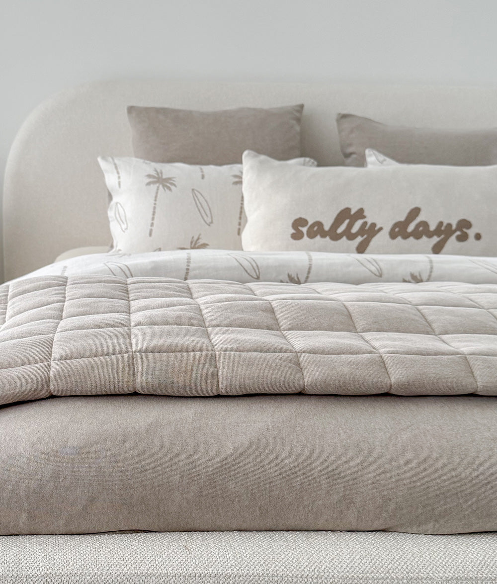 Dune quilt laid across a bed dressed in ivory and natural bedding