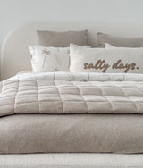 Dune quilt laid across a bed dressed in ivory and natural bedding