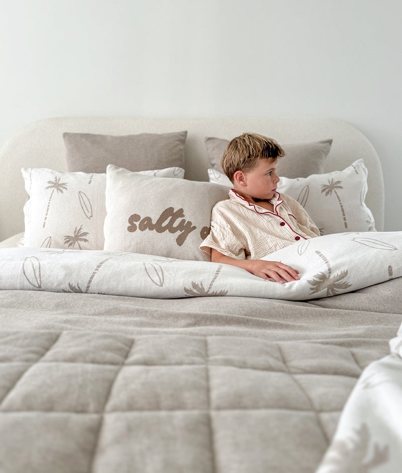 Child sitting up in bed against a Salty Days pillowcase and palm print pillowcases