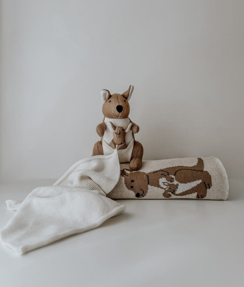 Kangaroo baby comforter snuggly with its white cuddle cloth spread in front of a rolled Kangaroo blanket