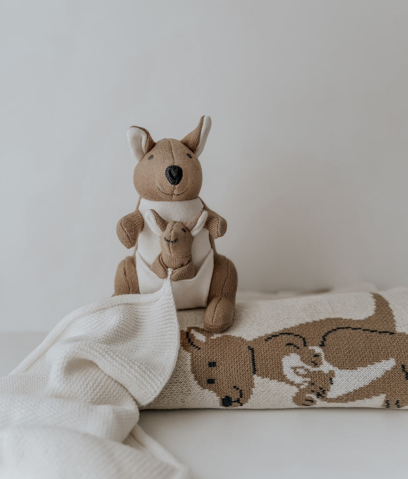 Kangaroo baby comforter snuggly on a rolled Kangaroo knitted baby blanket against a white wall