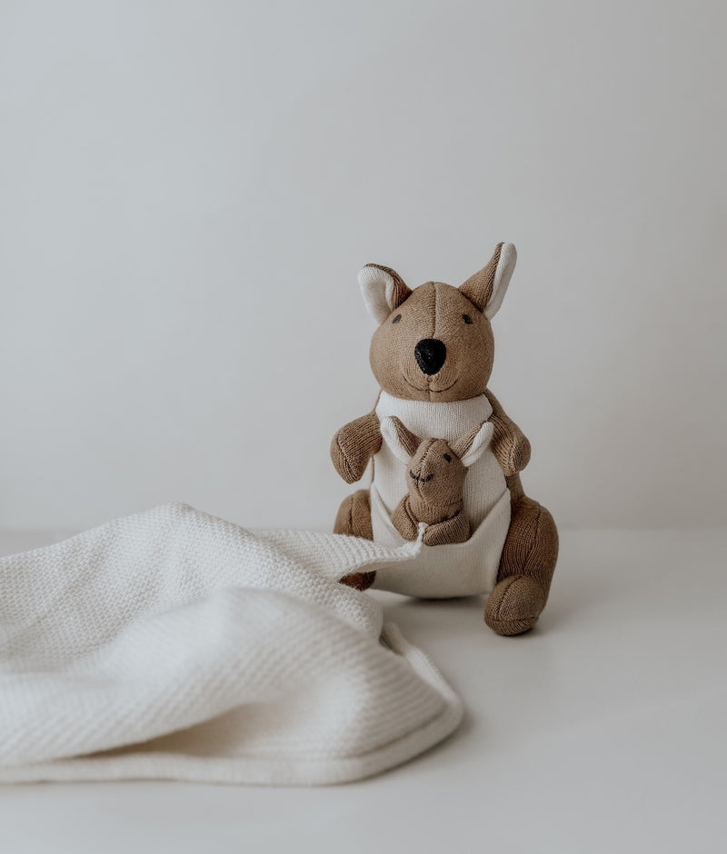 Kangaroo baby comforter snuggly with a joey in its pouch beside a soft white knit blanket