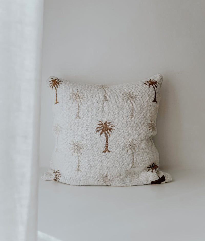 Palma palm cushion cover in ivory slub cotton on a bench beside a sheer curtain