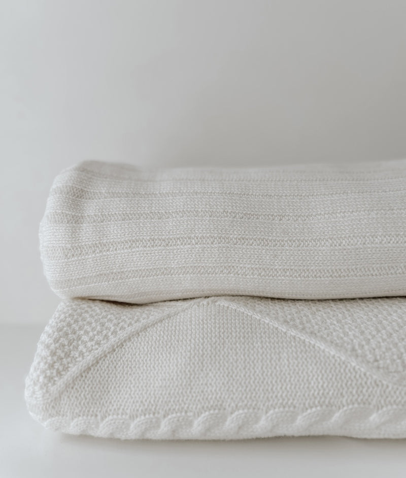 Ivory Corduroy lounge throw folded on top of the Ivory Diamante throw, showing ribbed and cable knits