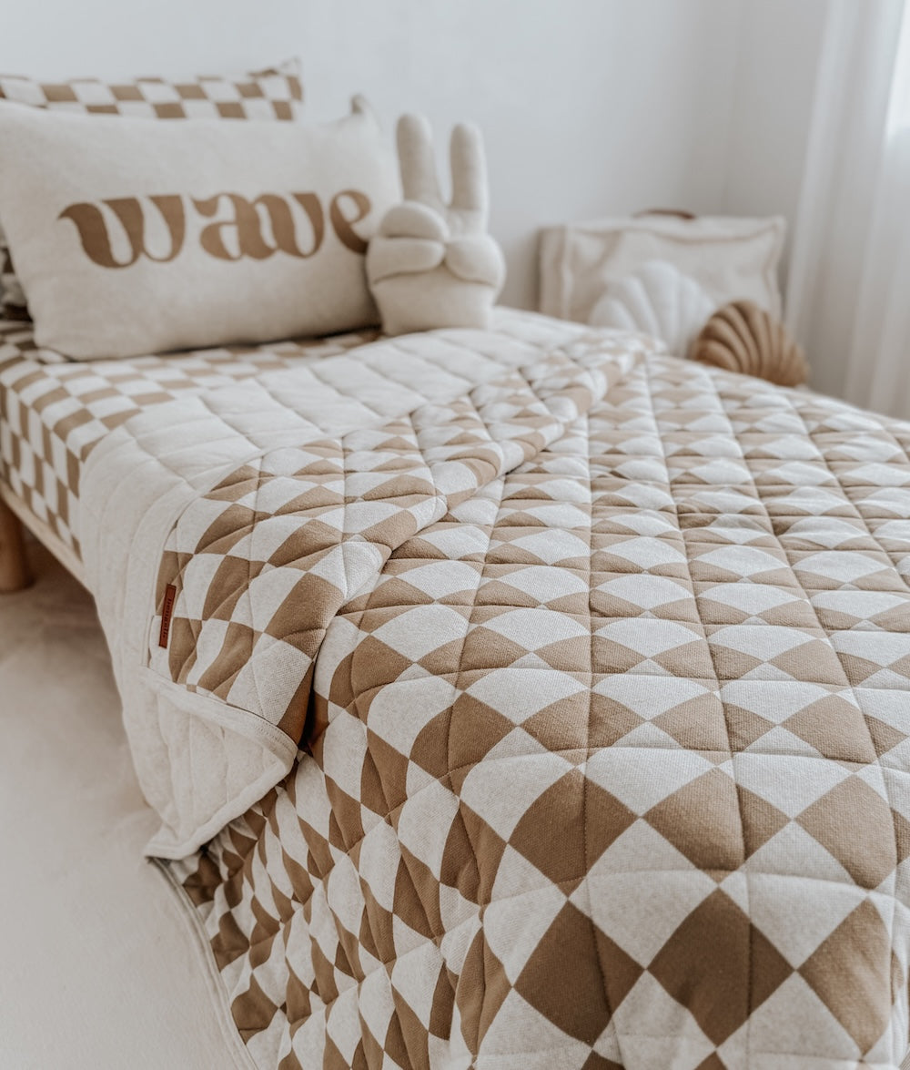 Khaki gingham quilt across a bed with a wave cushion at the head