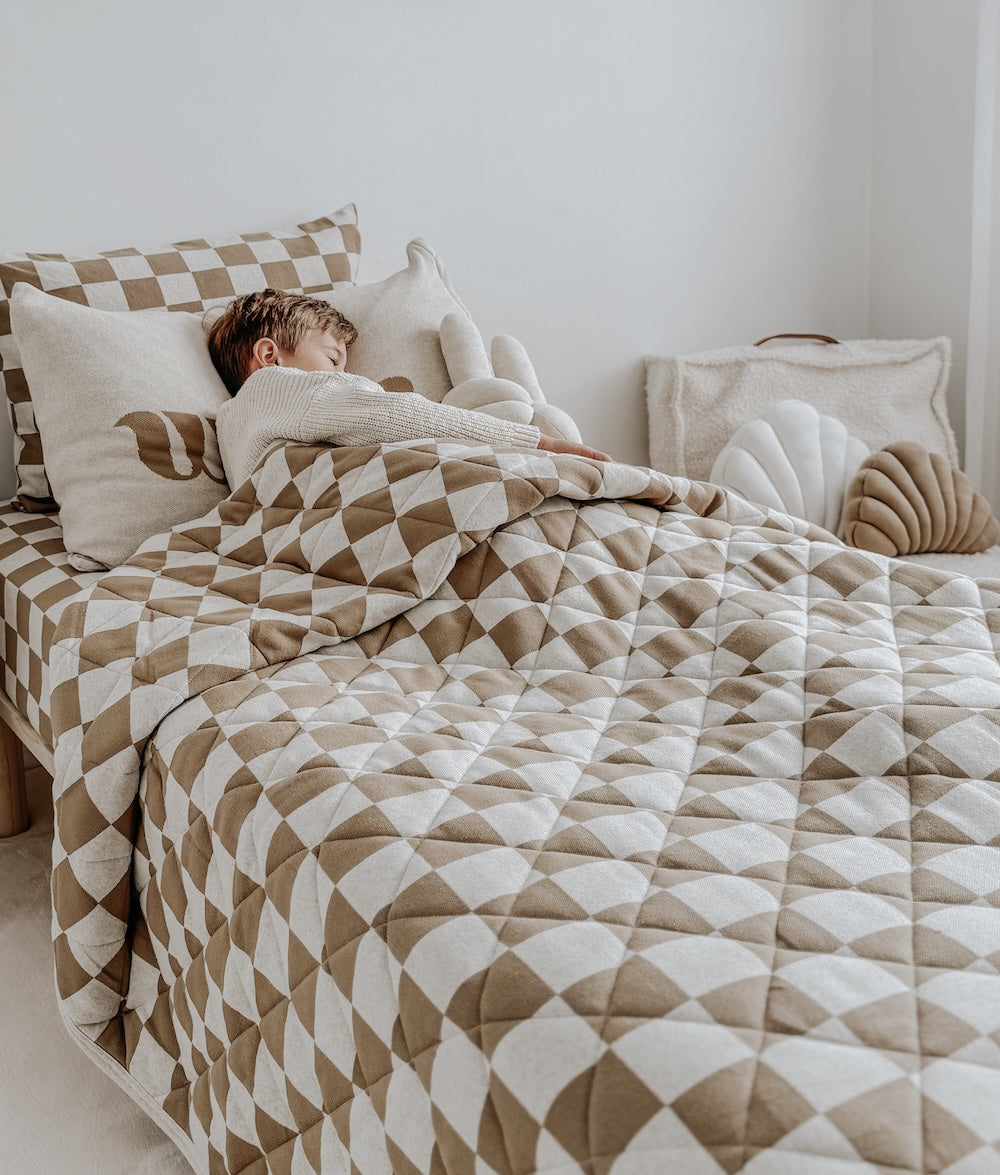 Made bed layered with the khaki gingham quilt, check pillows and a shell cushion