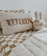 Wave lettering cushion and a bunny sherpa cushion on a bed with khaki gingham bedding