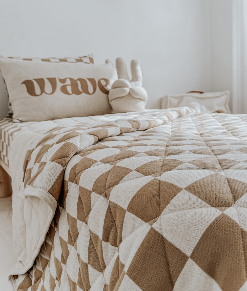 Khaki gingham quilt on a bed with a wave lettering cushion and a bunny sherpa cushion