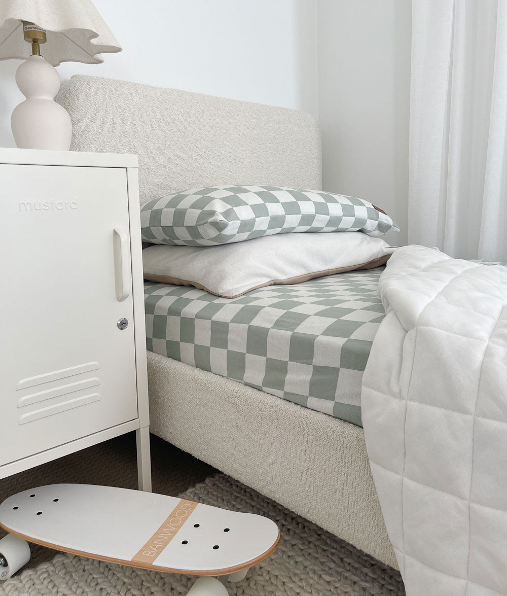 Sage Gingham jersey fitted sheet on a boucle bed with matching pillowcase, white quilt and a mini skateboard