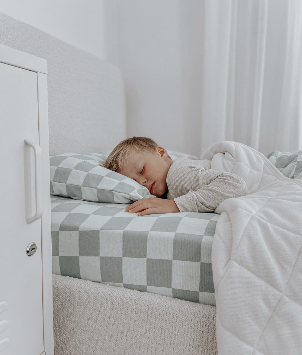 Child asleep on a Sage Gingham jersey cotton fitted sheet with a matching pillowcase and white quilt