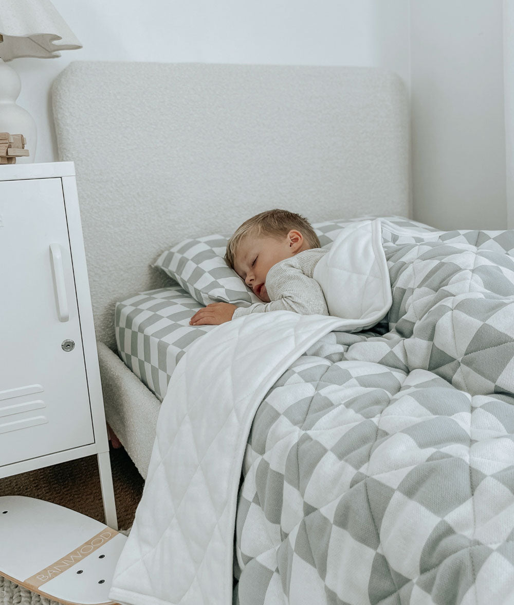 Child asleep under a Sage Gingham reversible cotton quilt on a matching Sage Gingham fitted sheet