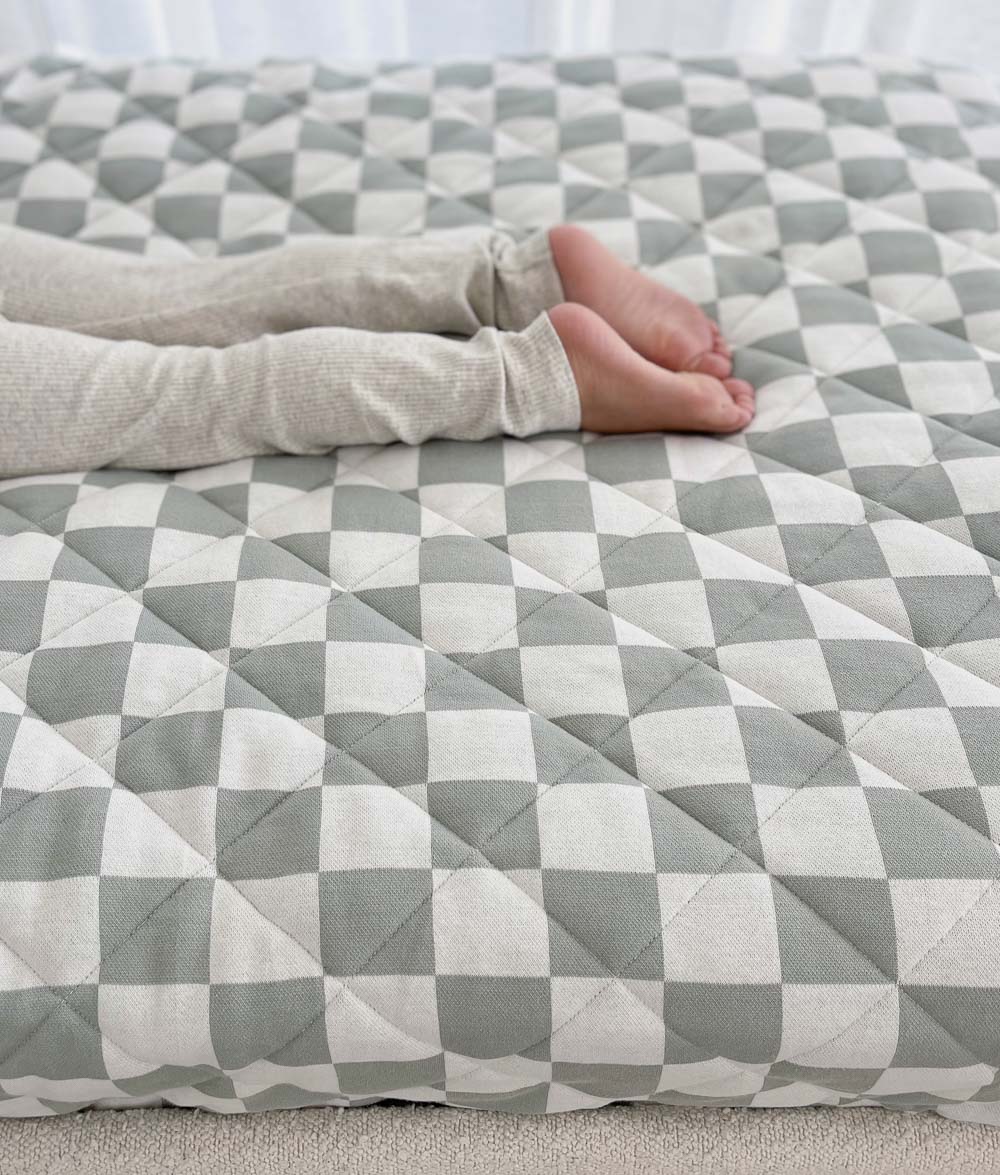 Child's feet resting on a quilted Sage Gingham reversible cotton quilt