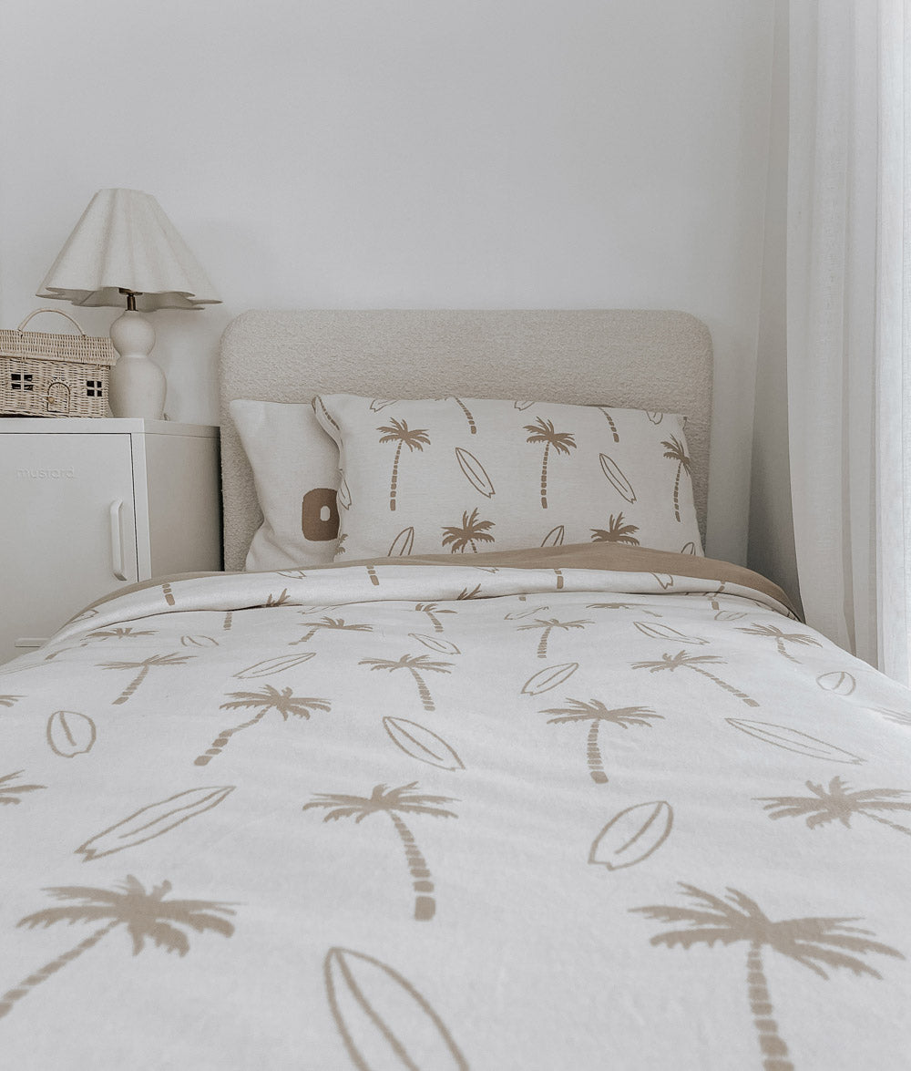 Single bed dressed in a natural Surfing Palm kids duvet cover and matching pillowcases beside a white bedside table