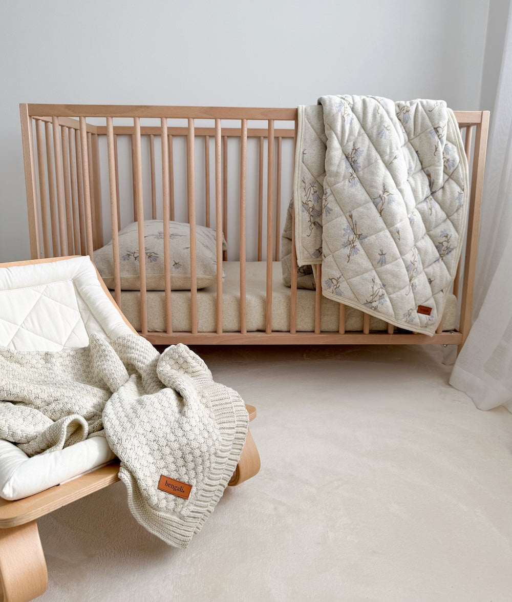 Cotton baby blanket draped over a timber baby bouncer in front of a cot