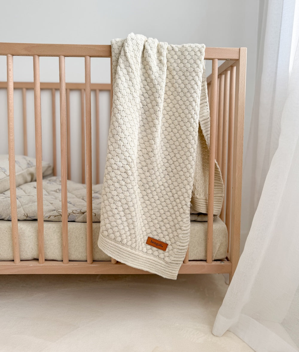 Vanilla Marle Pebble cotton baby blanket hung over the rail of a timber cot