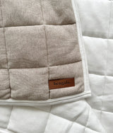 Corner of the dune quilt turned back to show the plain ivory reverse and leather Bengali tab