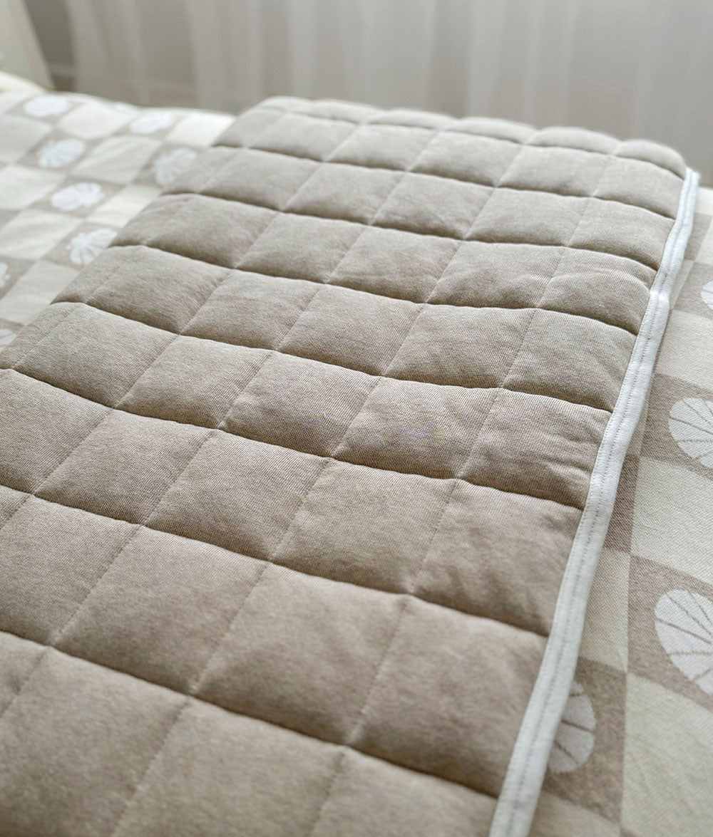 Dune quilted cot blanket folded over the side of a cot with shell check bedding beneath