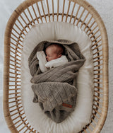 Newborn wrapped in the stone shell stitch blanket inside a rattan bassinet