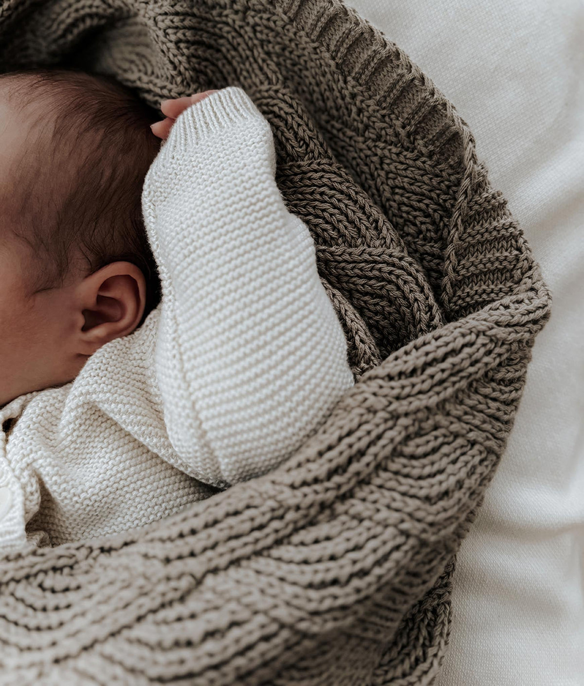 Newborn tucked under the stone shell stitch blanket on ivory bedding