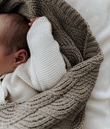 Newborn tucked under the stone shell stitch blanket on ivory bedding