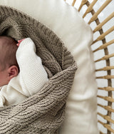 Newborn swaddled in the stone shell stitch blanket in a rattan bassinet