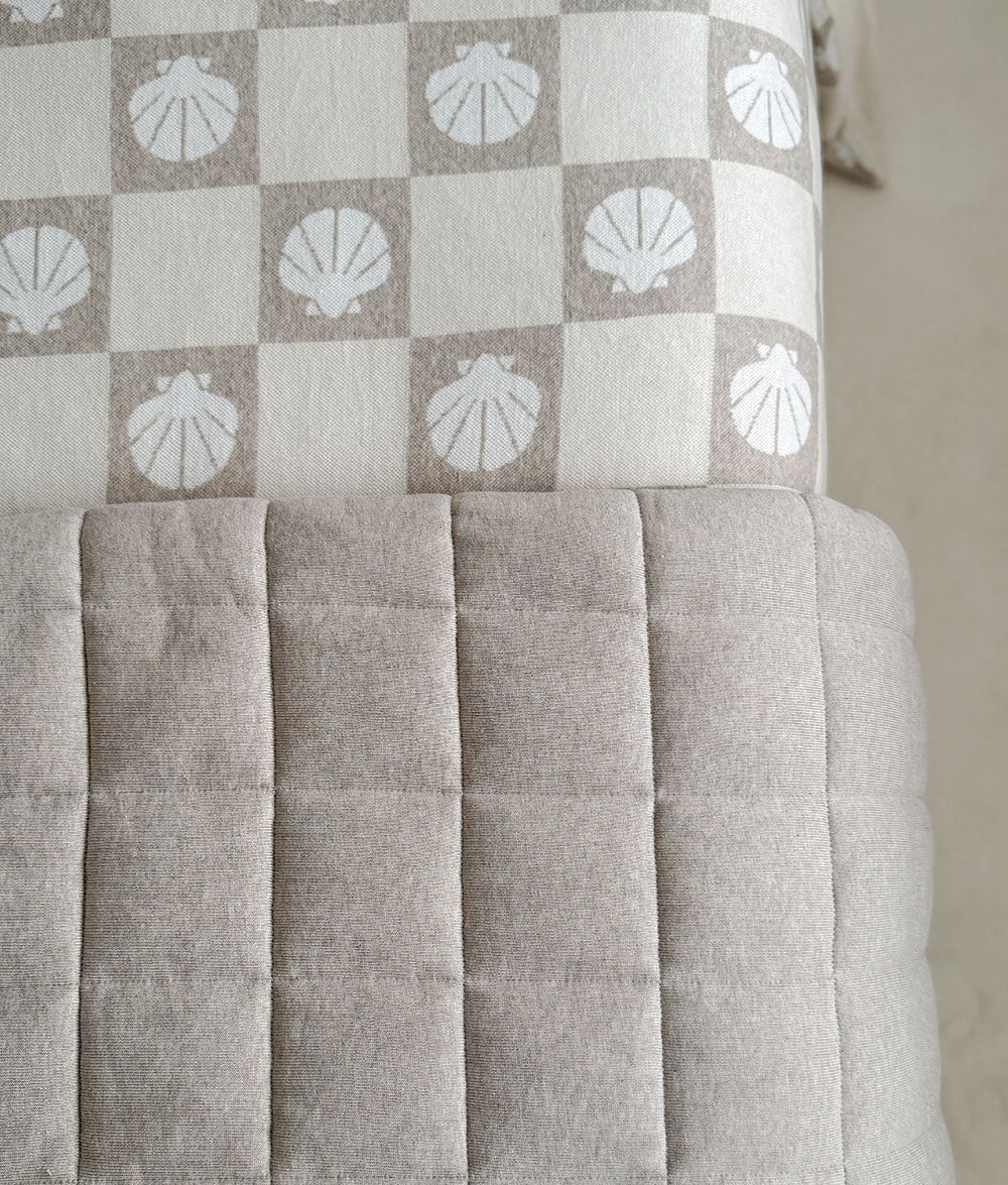 Close-up of the dune quilted stitching beside shell check bedding