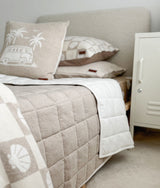 Dune quilt draped over the end of a bed dressed in shell check bedding
