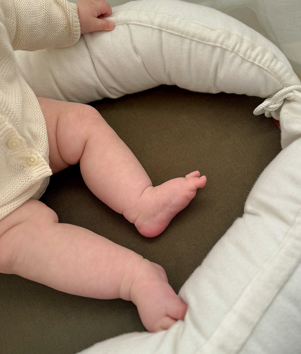 Baby resting inside the olive baby lounger with the ivory cushioned sides around them