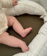 Baby resting inside the olive baby lounger with the ivory cushioned sides around them