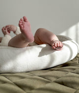 Baby feet on the ivory edge of the lounger nest above an olive quilted bedspread