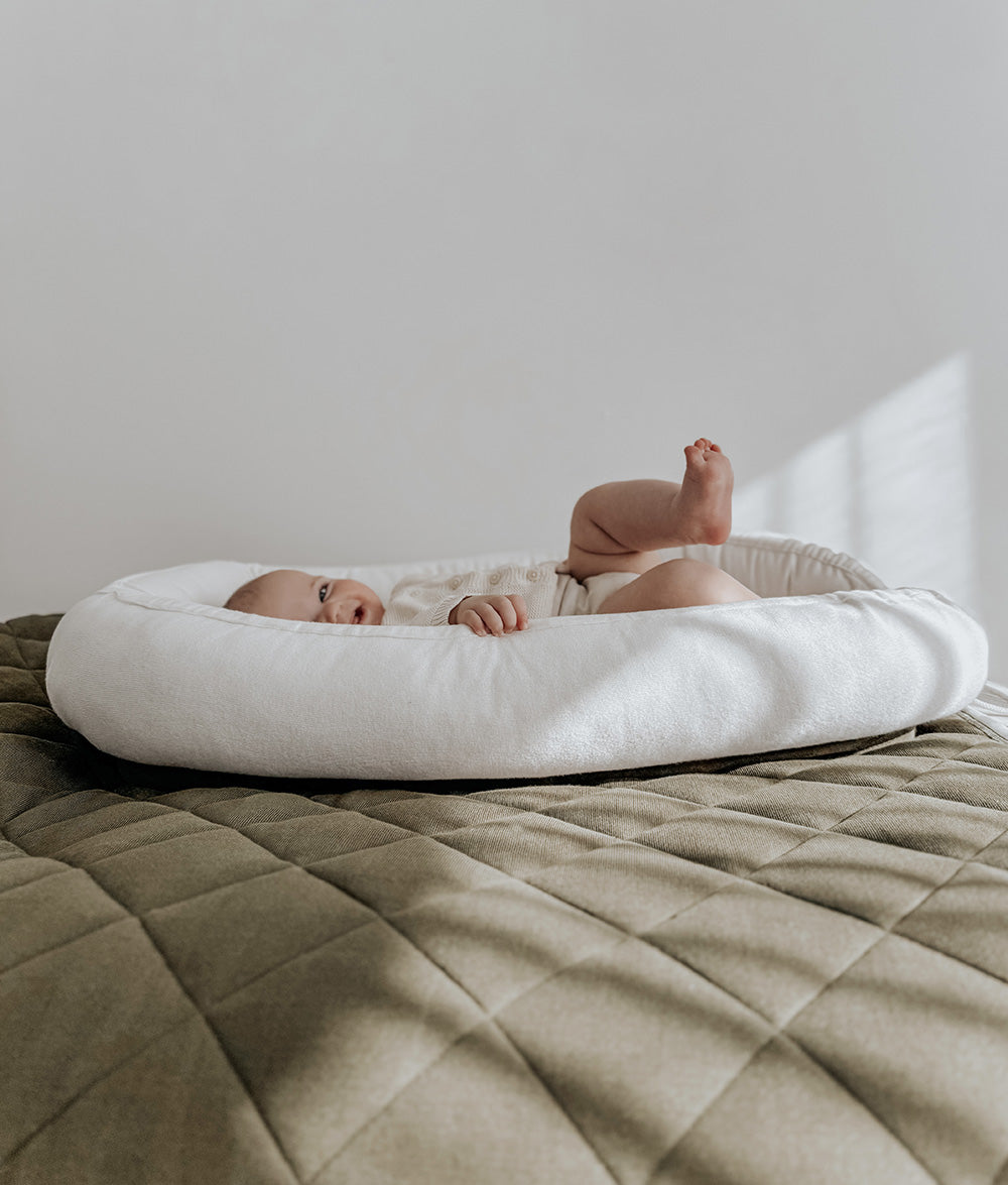 Baby lying in the olive and ivory lounger nest on an olive quilted bedspread