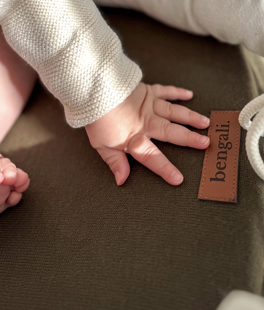 Baby hand on the olive lounger base beside the leather Bengali tab