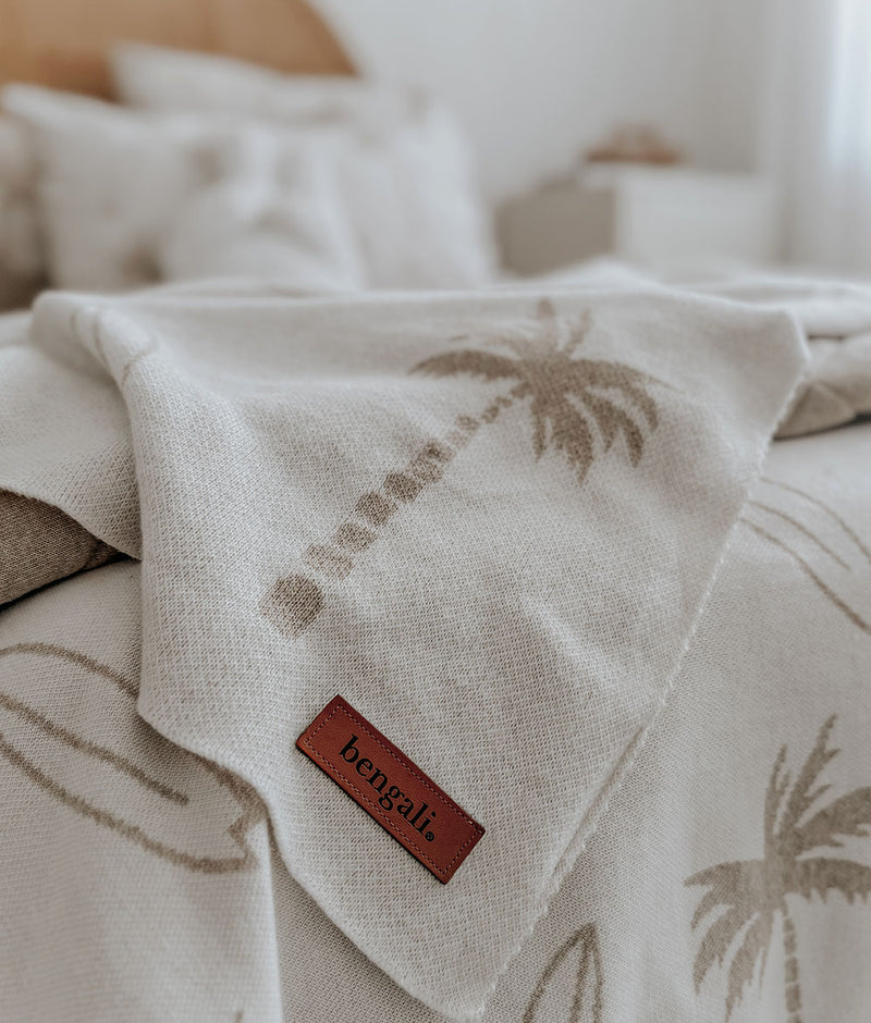 Close-up of a dune Surfing Palm knitted cotton baby blanket with leather label, on palm print bedding