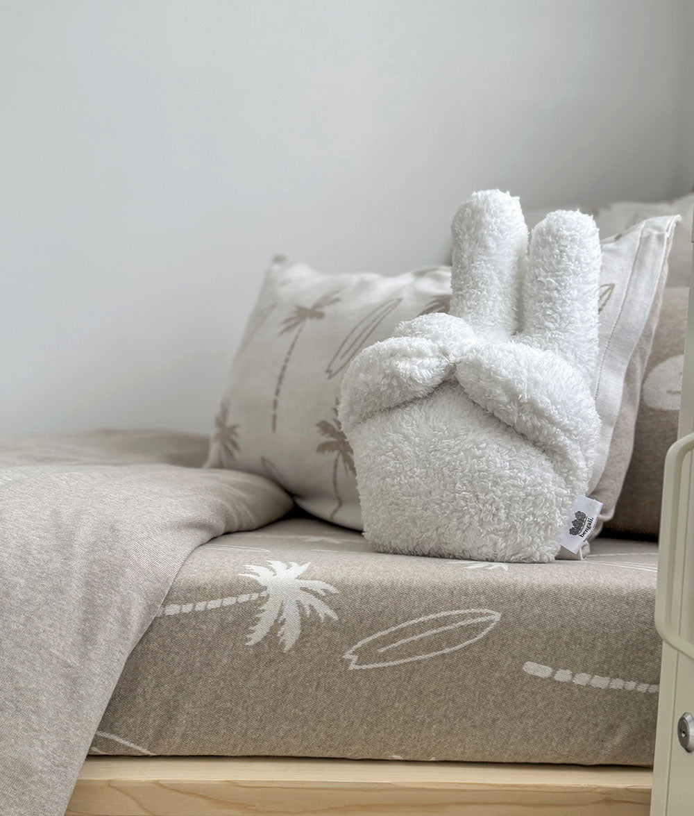 White sherpa bunny cushion sitting on the dune palm fitted sheet with palm pillows behind