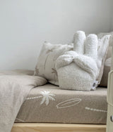 White sherpa bunny cushion sitting on the dune palm fitted sheet with palm pillows behind