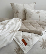 Dune palm print euro pillowcases with a quilted palm throw folded across the bed