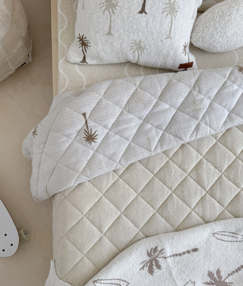 Overhead view of a Coastal Marle fitted sheet beneath quilted palm print bedding and palm tree cushions
