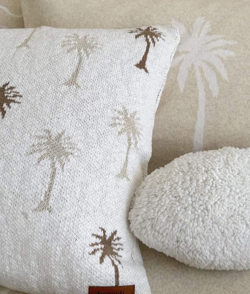 Close-up of the Palma cushion cover's textured ivory slub and palm trees beside a Sherpa cushion