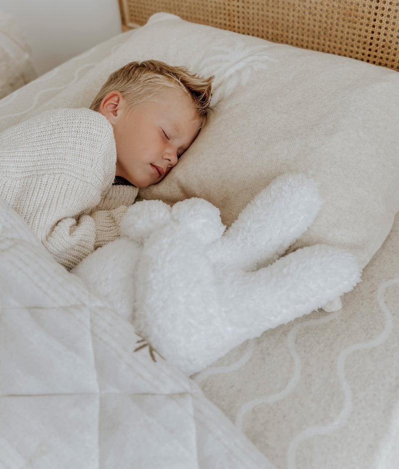 Child asleep beside the ivory Peace Sherpa kids cushion on a Coastal Marle jersey fitted sheet