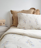Floral pillow resting in front of khaki frill euro pillowcases on a made bed