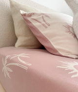 Cream palm and sun print pillow resting on a soft pink fitted sheet