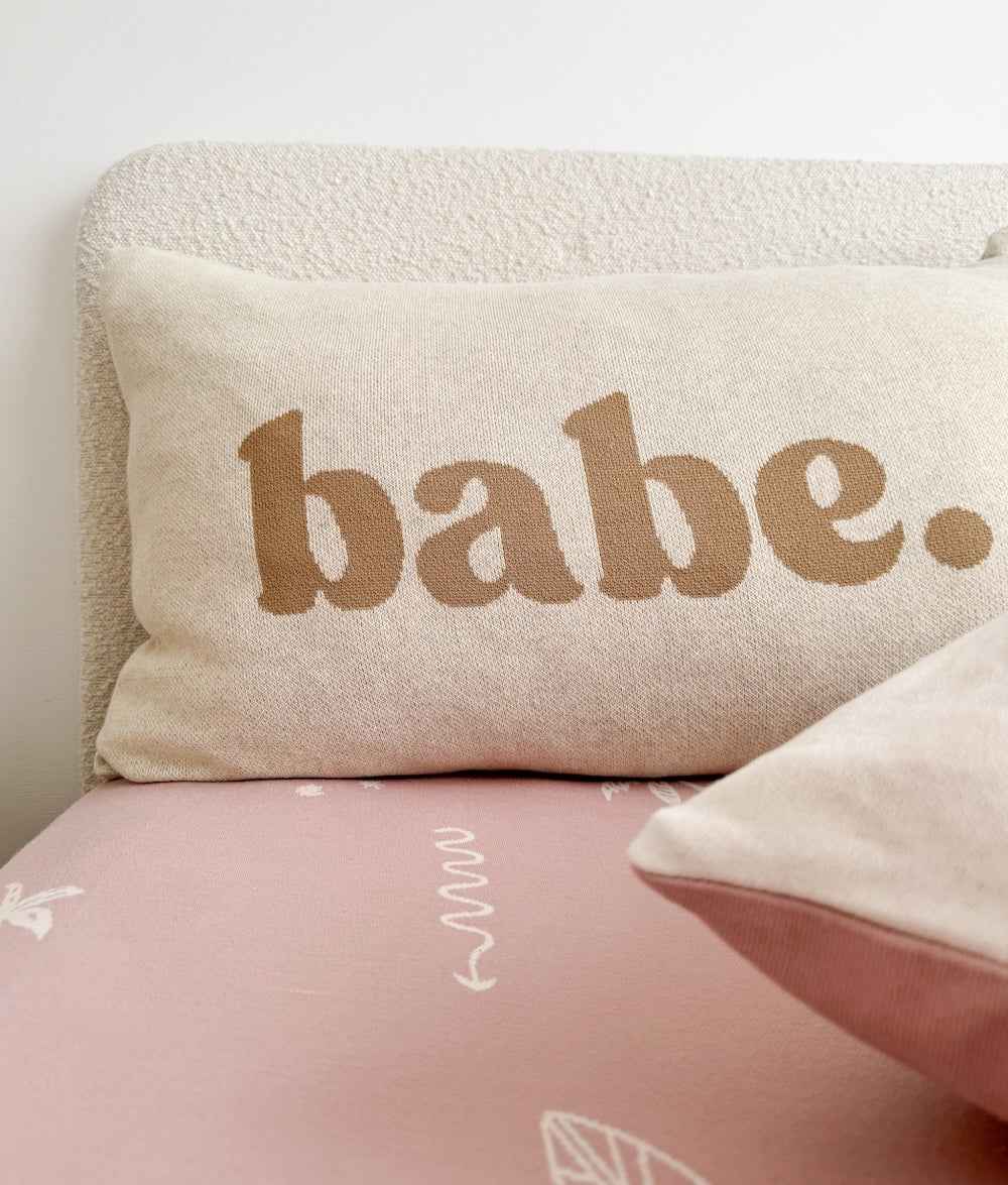 Babe pillowcase in khaki lettering against a boucle headboard on a pink sheet