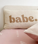 Babe pillowcase in khaki lettering against a boucle headboard on a pink sheet