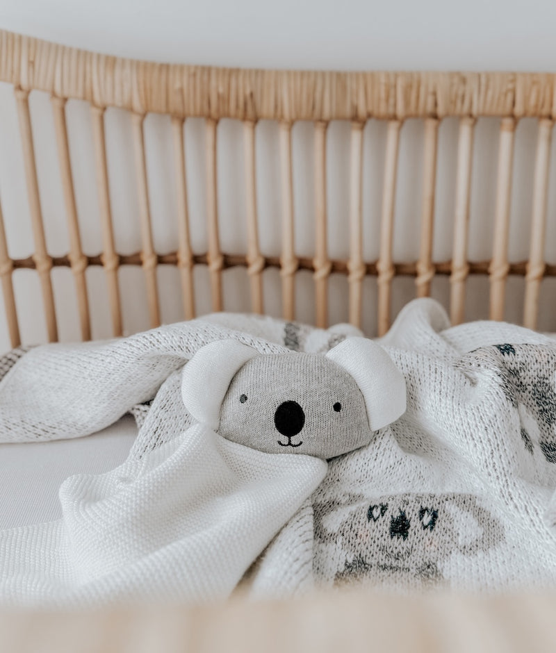 Koala baby comforter snuggly lying on a koala knit blanket in a rattan bassinet