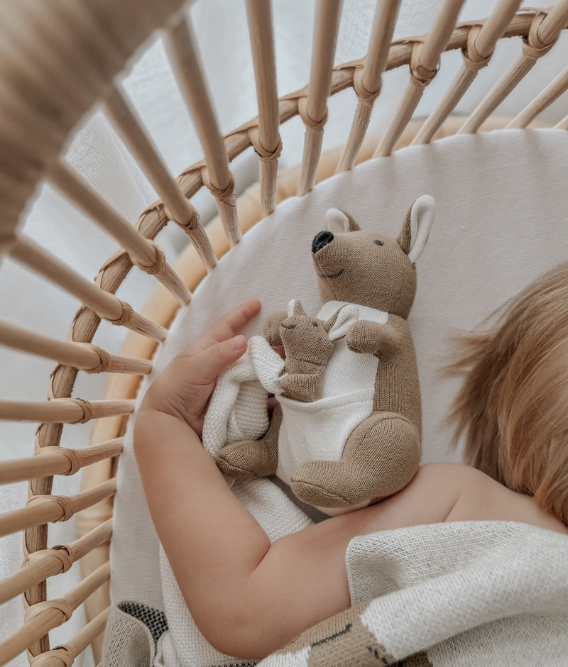Baby in a rattan bassinet cuddling the Kangaroo baby comforter snuggly, a joey tucked in its pouch