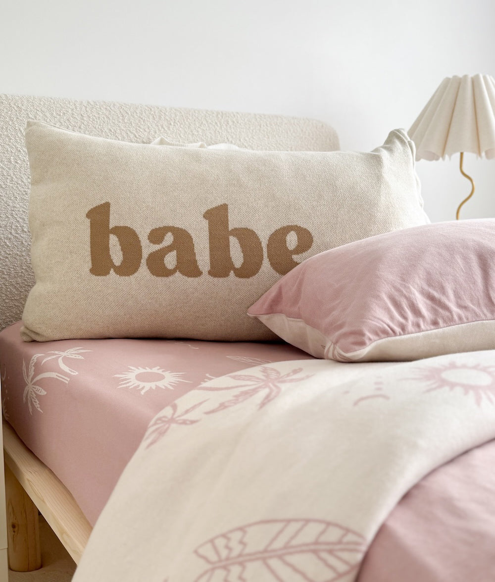 Natural marle Babe pillowcase in khaki lettering on a bed with a soft pink fitted sheet