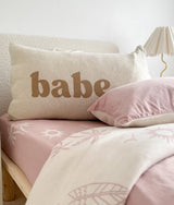 Natural marle Babe pillowcase in khaki lettering on a bed with a soft pink fitted sheet