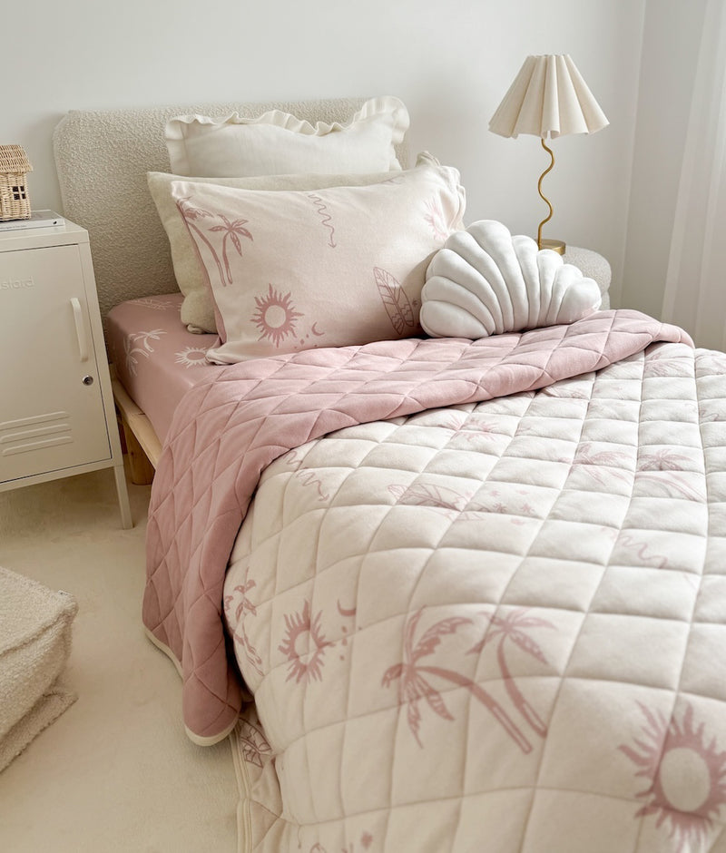 Ivory Frill euro pillowcases behind a palm print pillowcase and white shell cushion on a blush quilt