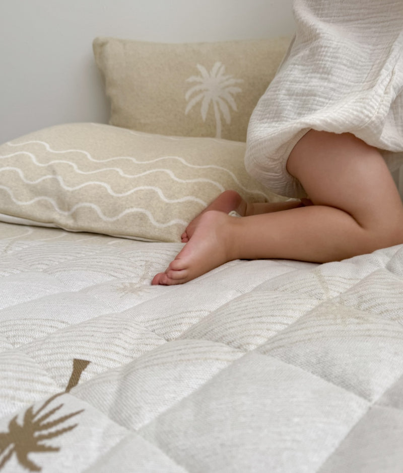 Child kneeling on a quilt beside the Aloha pillowcase turned to its wave print reverse